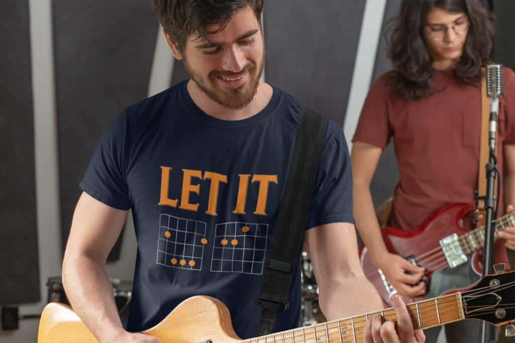 Lifestyle mockup of the witty, music-inspired Let It Be Musical Riddle print by Relateeble on a navy colored unisex/men's short sleeve tee