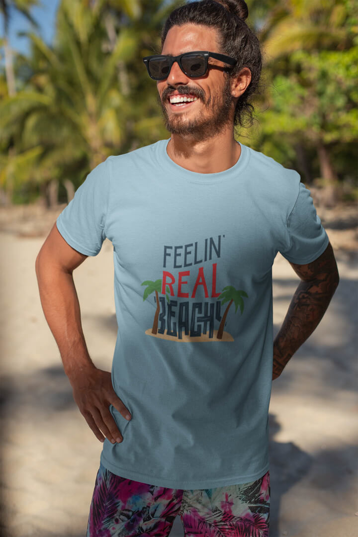 Lifestyle mockup of the witty, travel-inspired Feelin' Real Beachy print by Relateeble on an ice blue colored unisex/men's short sleeve tee