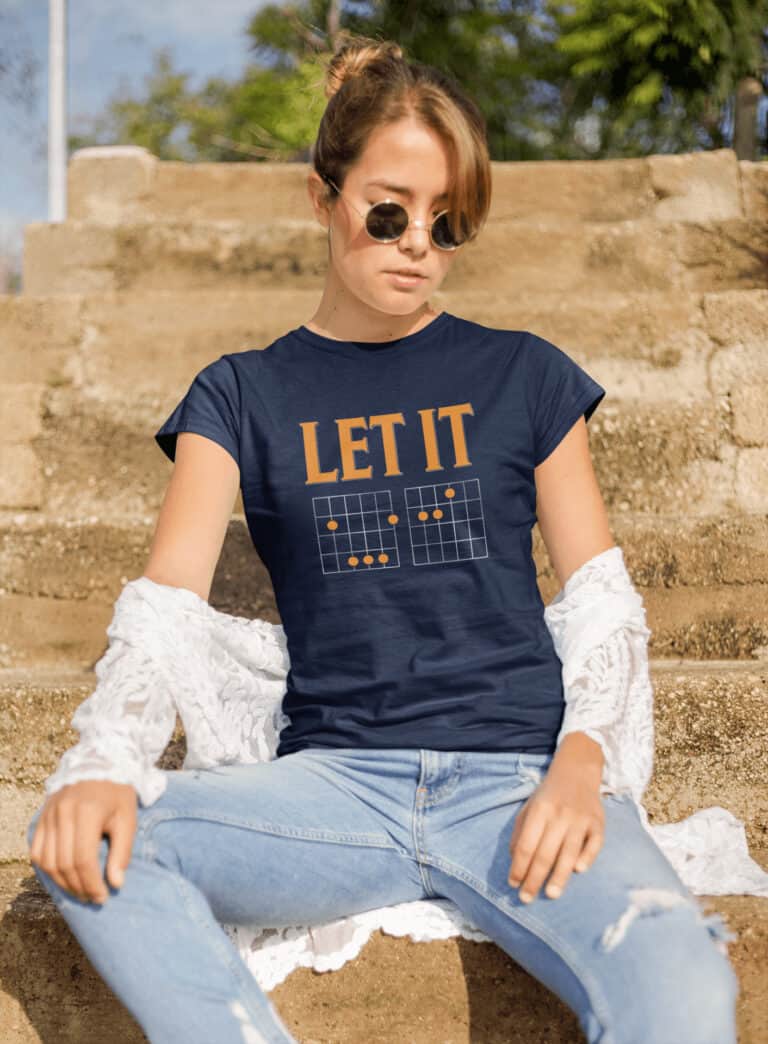 Lifestyle mockup of the witty, music-inspired Let It Be Musical Riddle print by Relateeble on a navy colored women's short sleeve tee