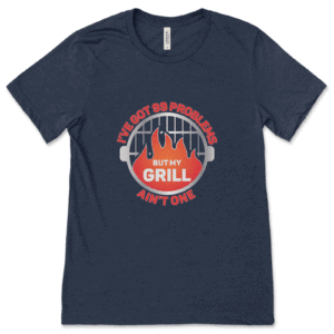 Product mockup of the funny, grilling-inspired 99 Problems, But My Grill Ain't One print by Relateeble on a navy colored unisex/men's short sleeve tee